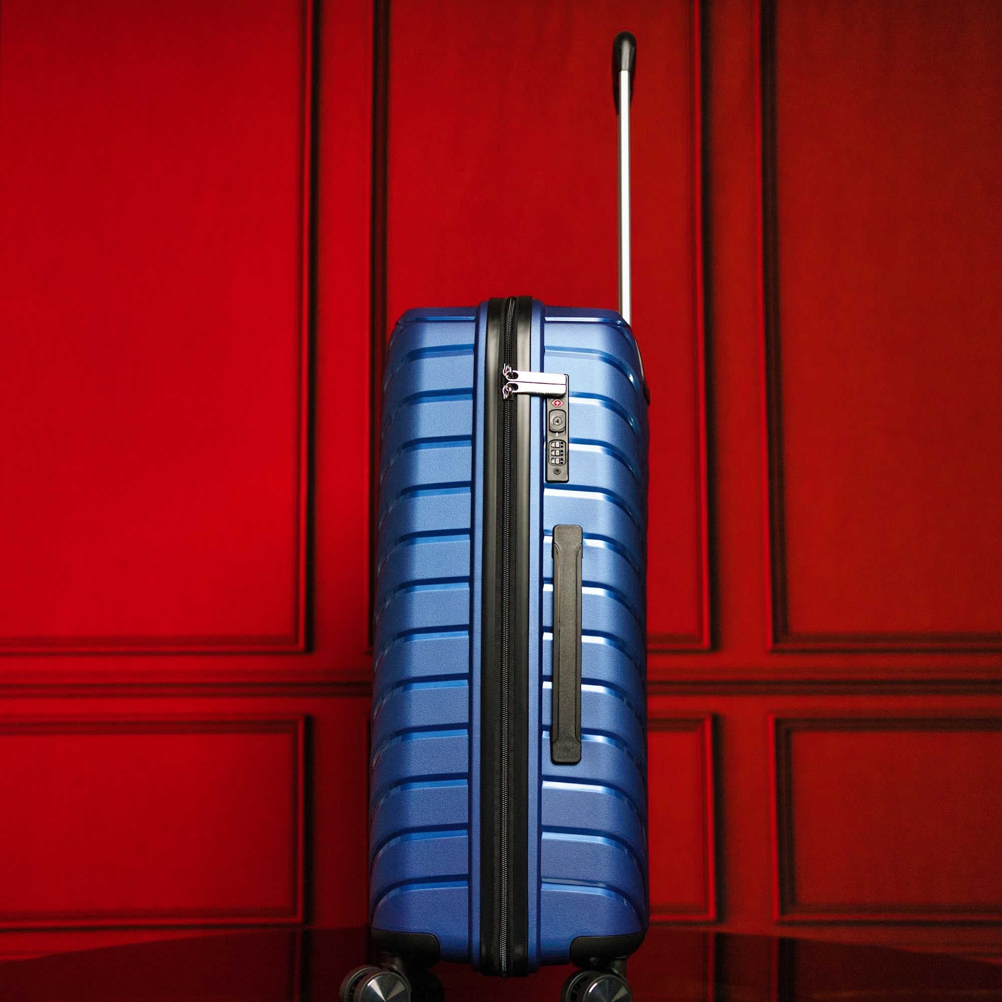 Blue suitcase with a black handle against a red paneled wall