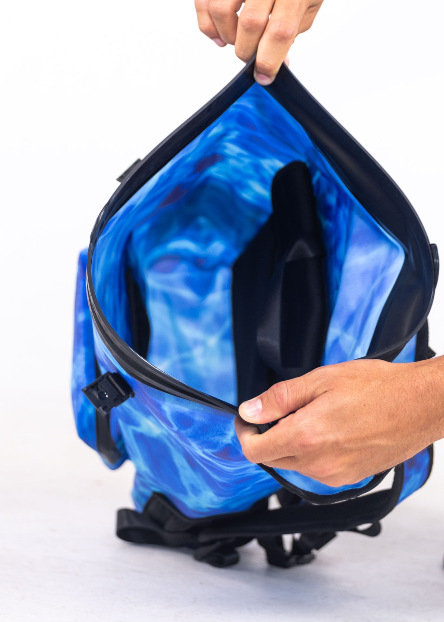 Blue cooler bag with black interior being held open by a hand on a white background