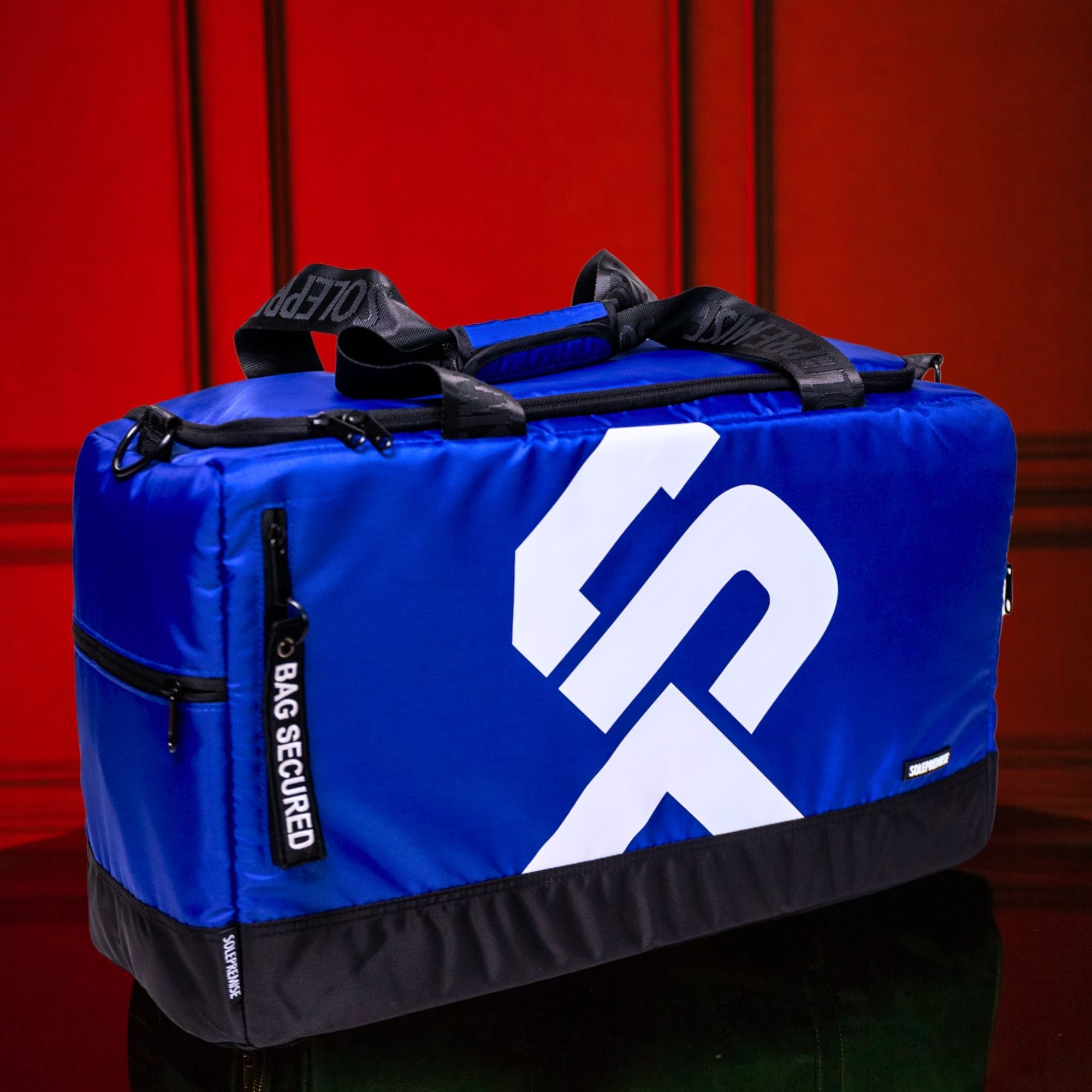 Blue duffel bag with a white logo on a red background
