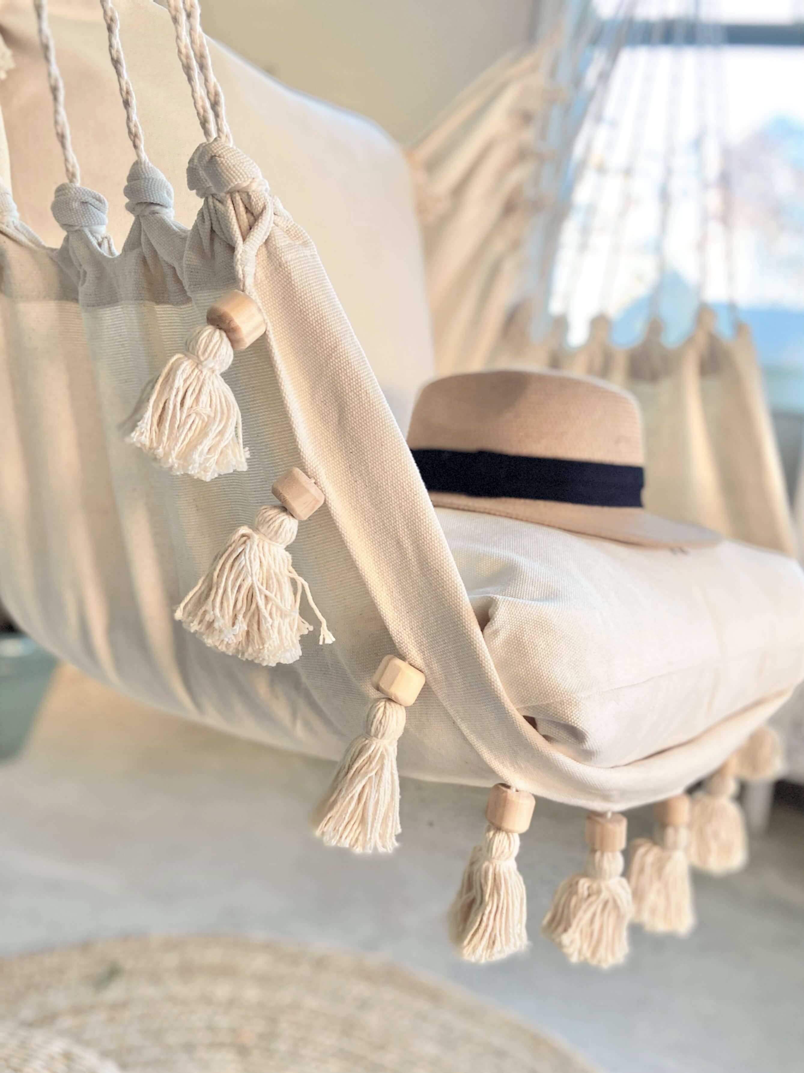 Beige hammock with tassels and a straw hat on a blurred beach background