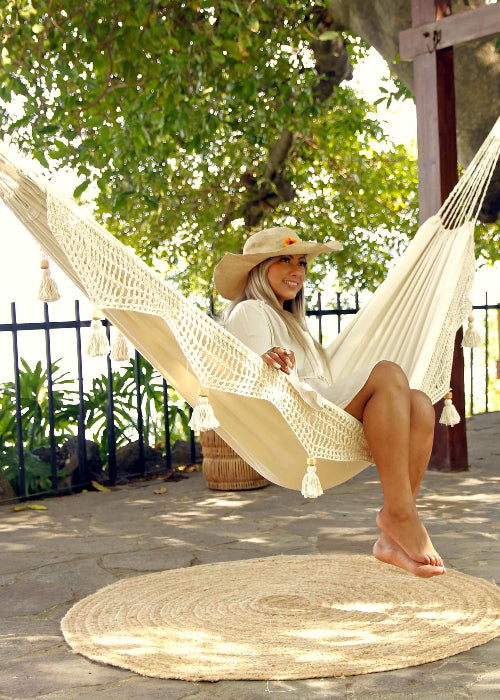 Woman sitting in a hammock on a patio with greenery in the background