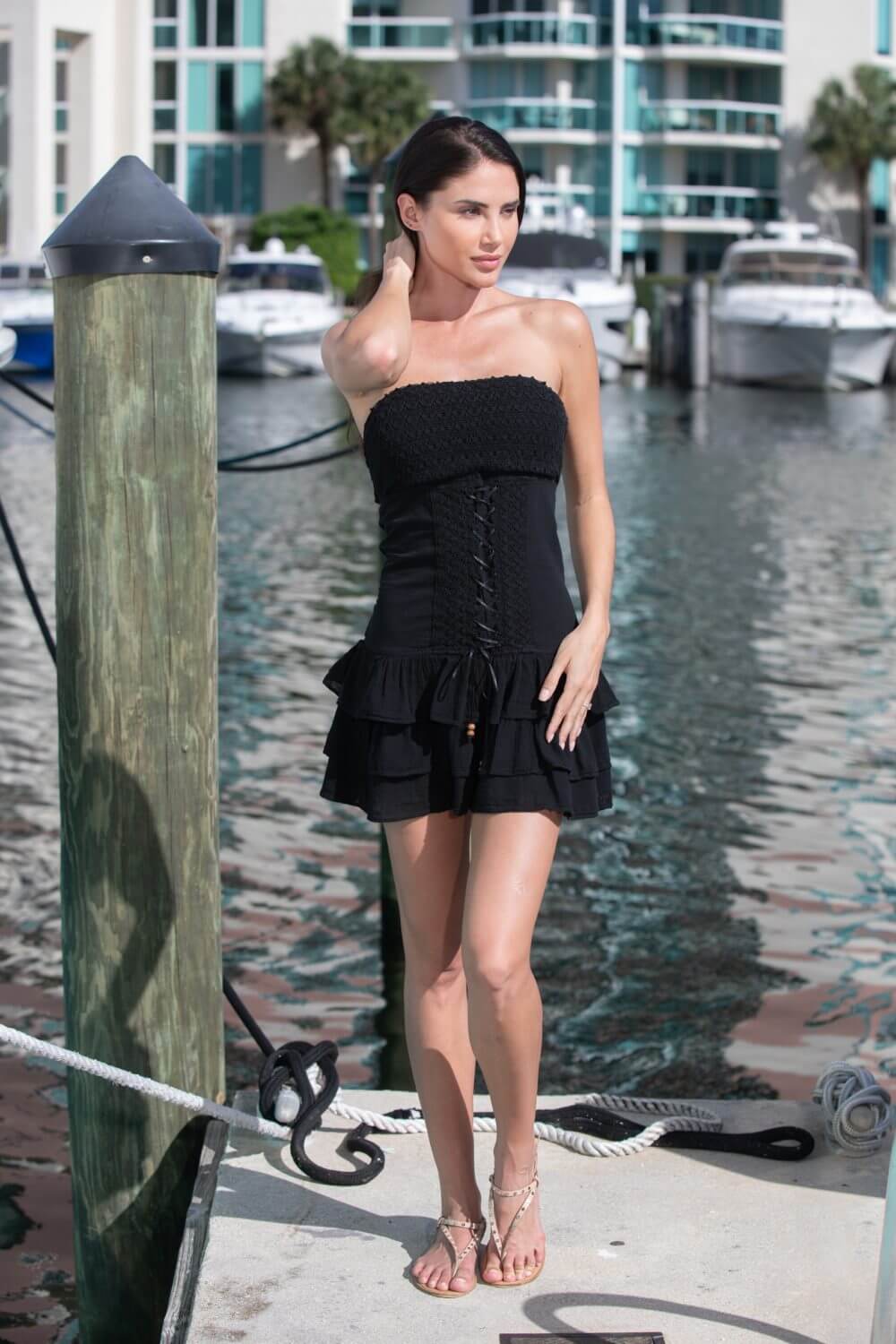 Woman in a black strapless dress standing by a dock with boats in the background