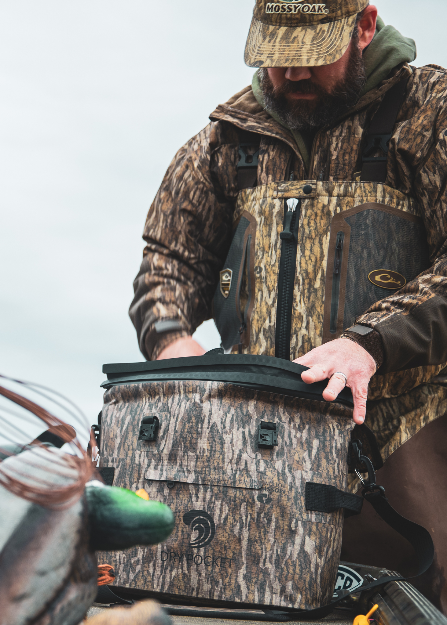 Man in camouflage gear opening a cooler with a Mossy Oak logo.