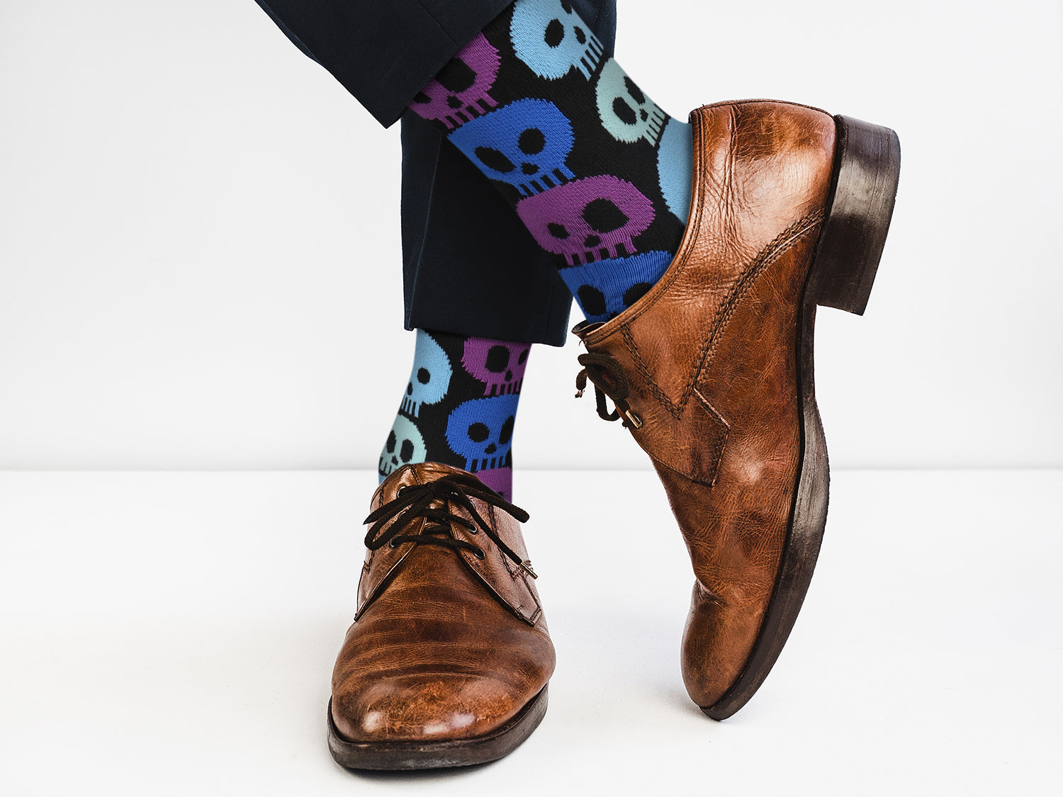 Brown leather shoes with colorful skull-patterned socks on a white background