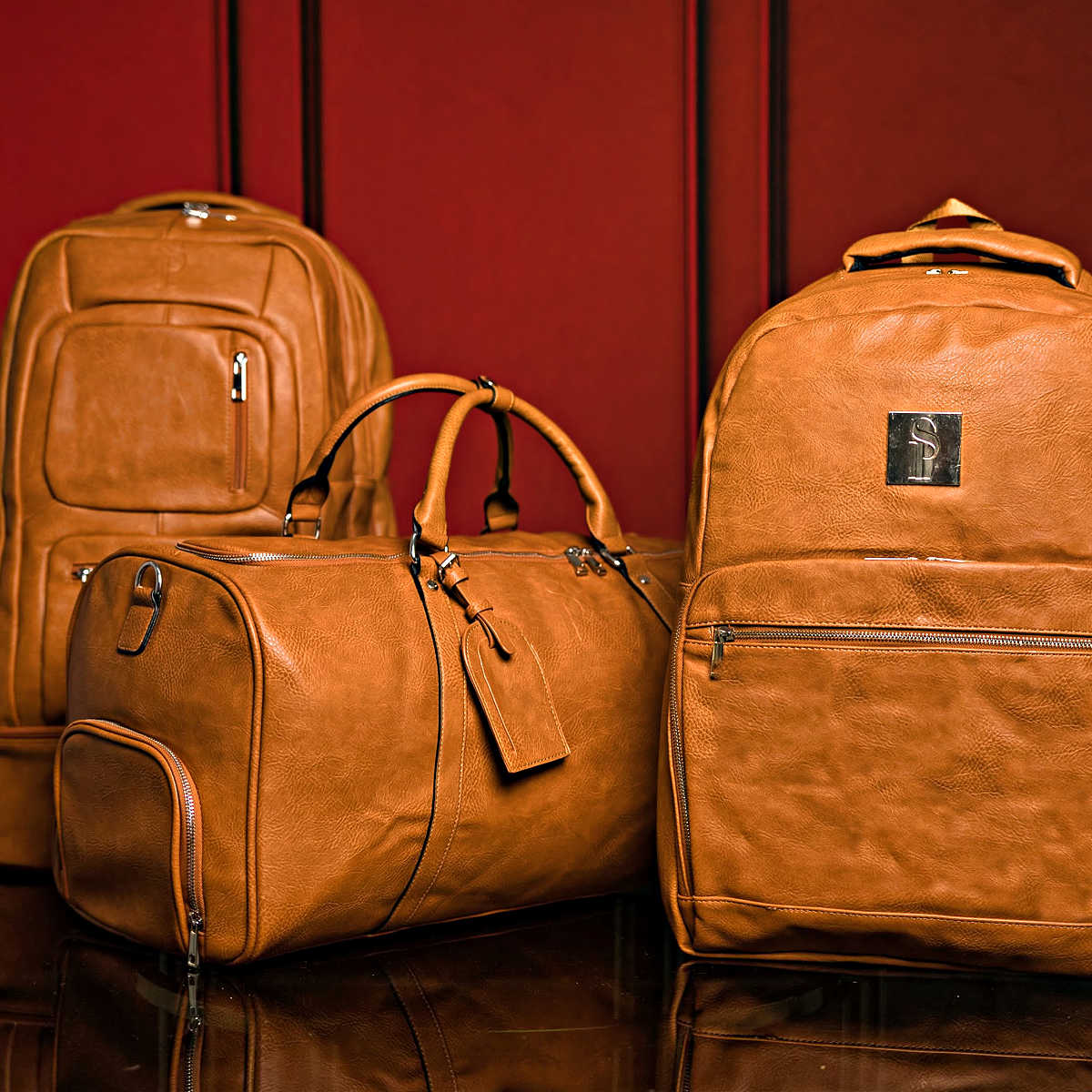 Three brown leather bags on a reflective surface with a red background