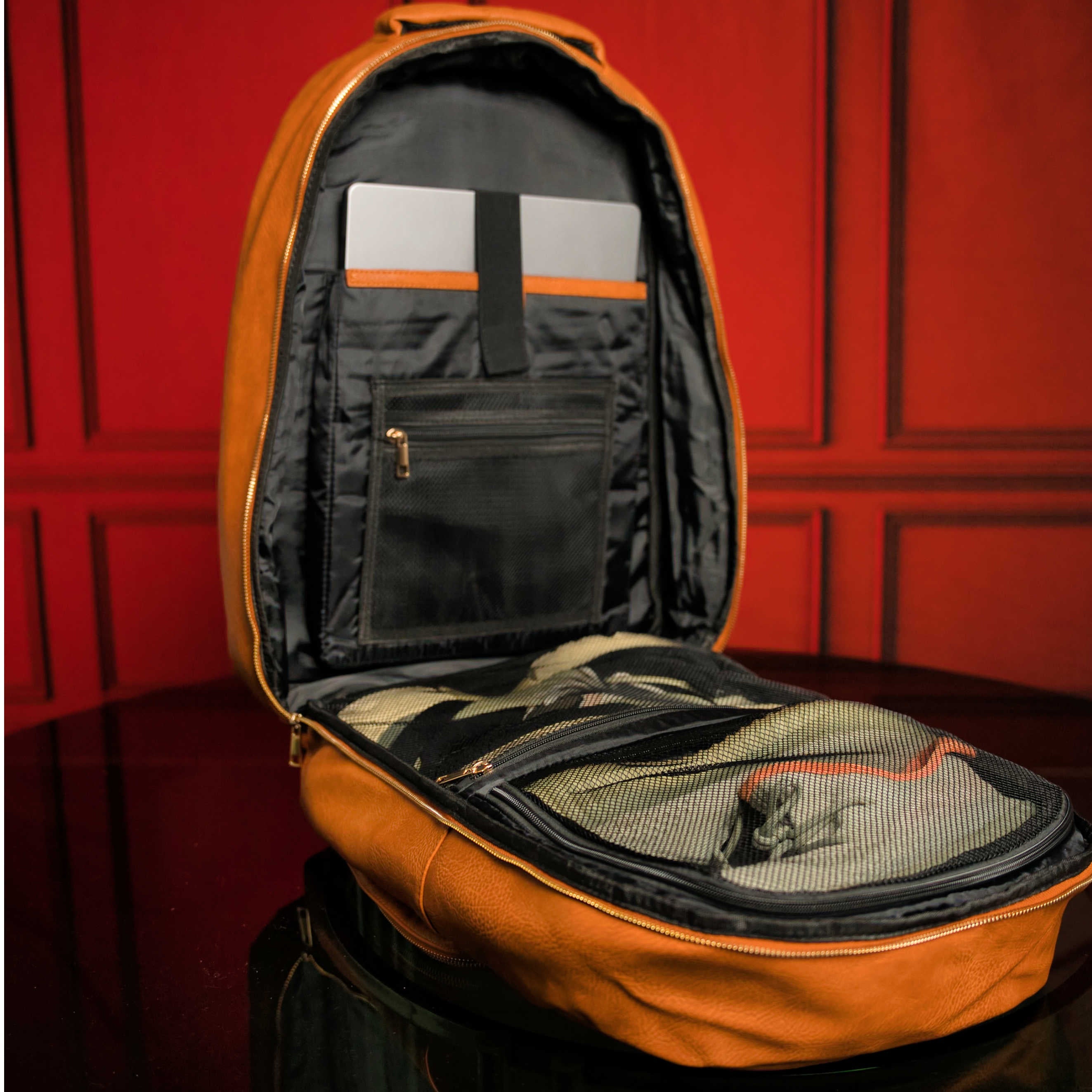 Orange backpack with open front compartment against a red paneled wall.