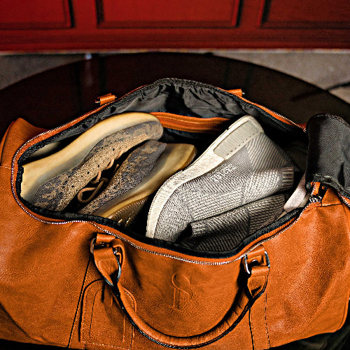 Brown leather duffel bag with shoes inside, against a red door background
