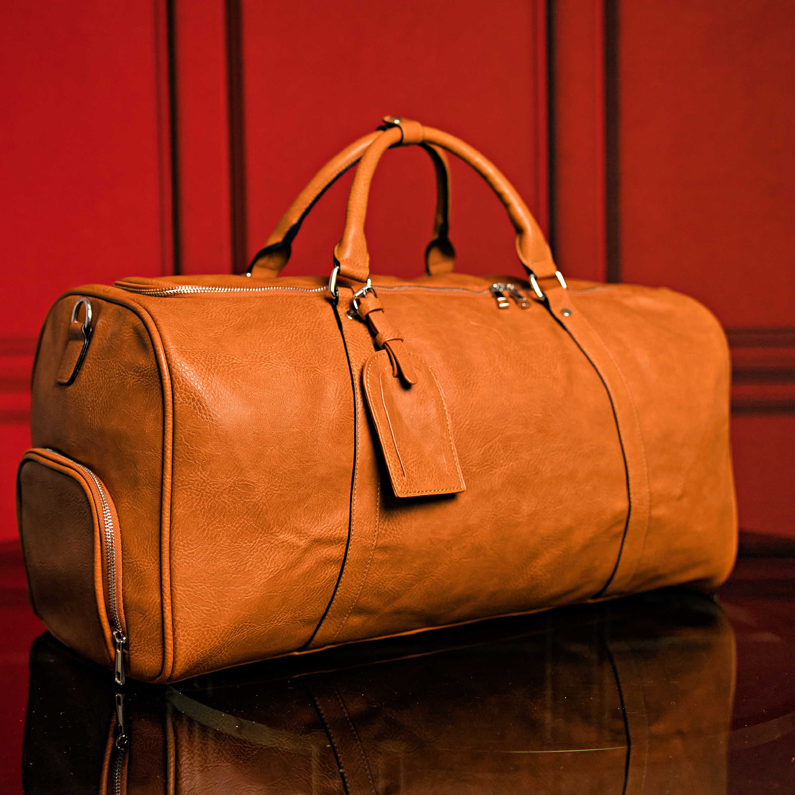 Brown leather duffel bag on a reflective surface with a red background