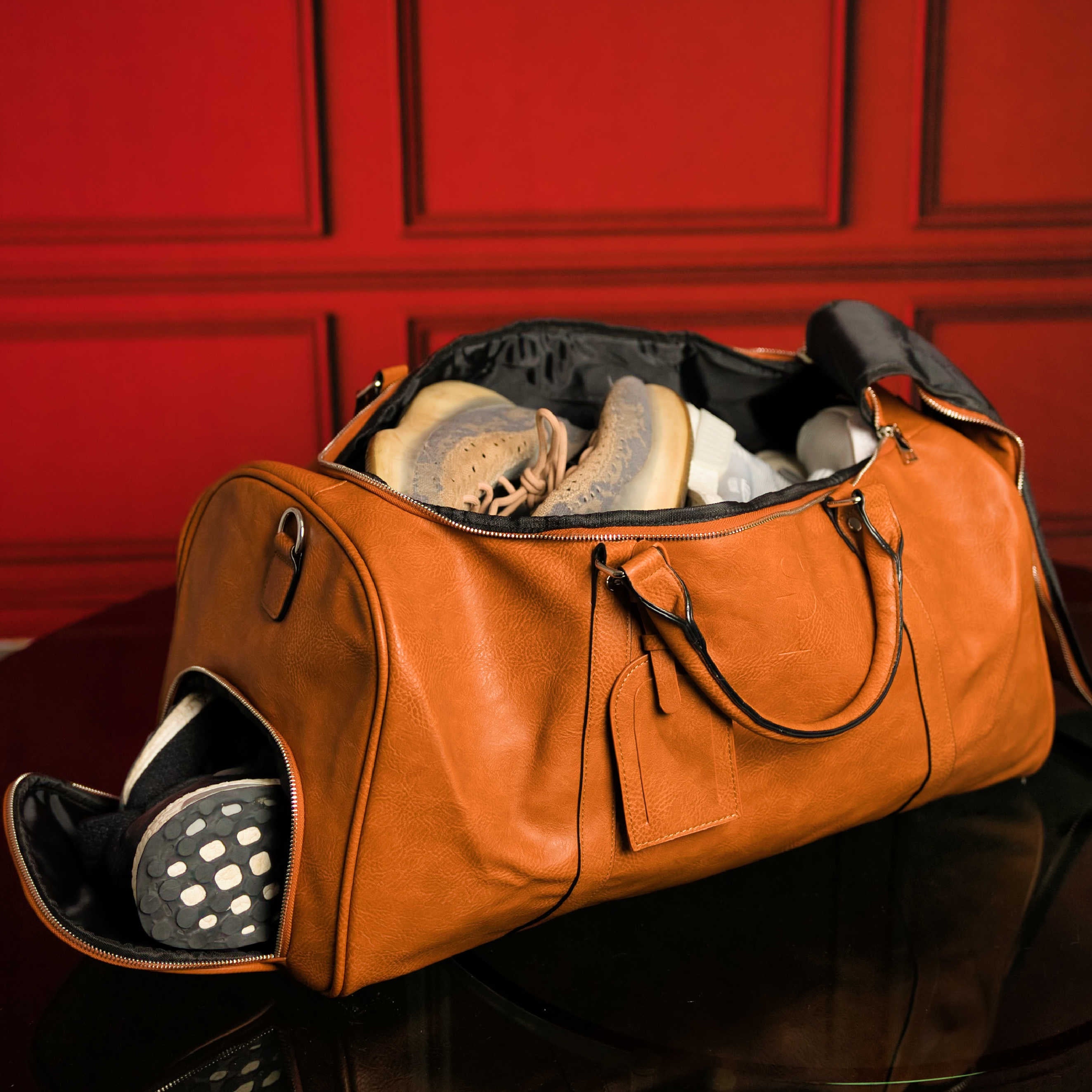 Brown leather duffel bag with shoes against a red paneled wall