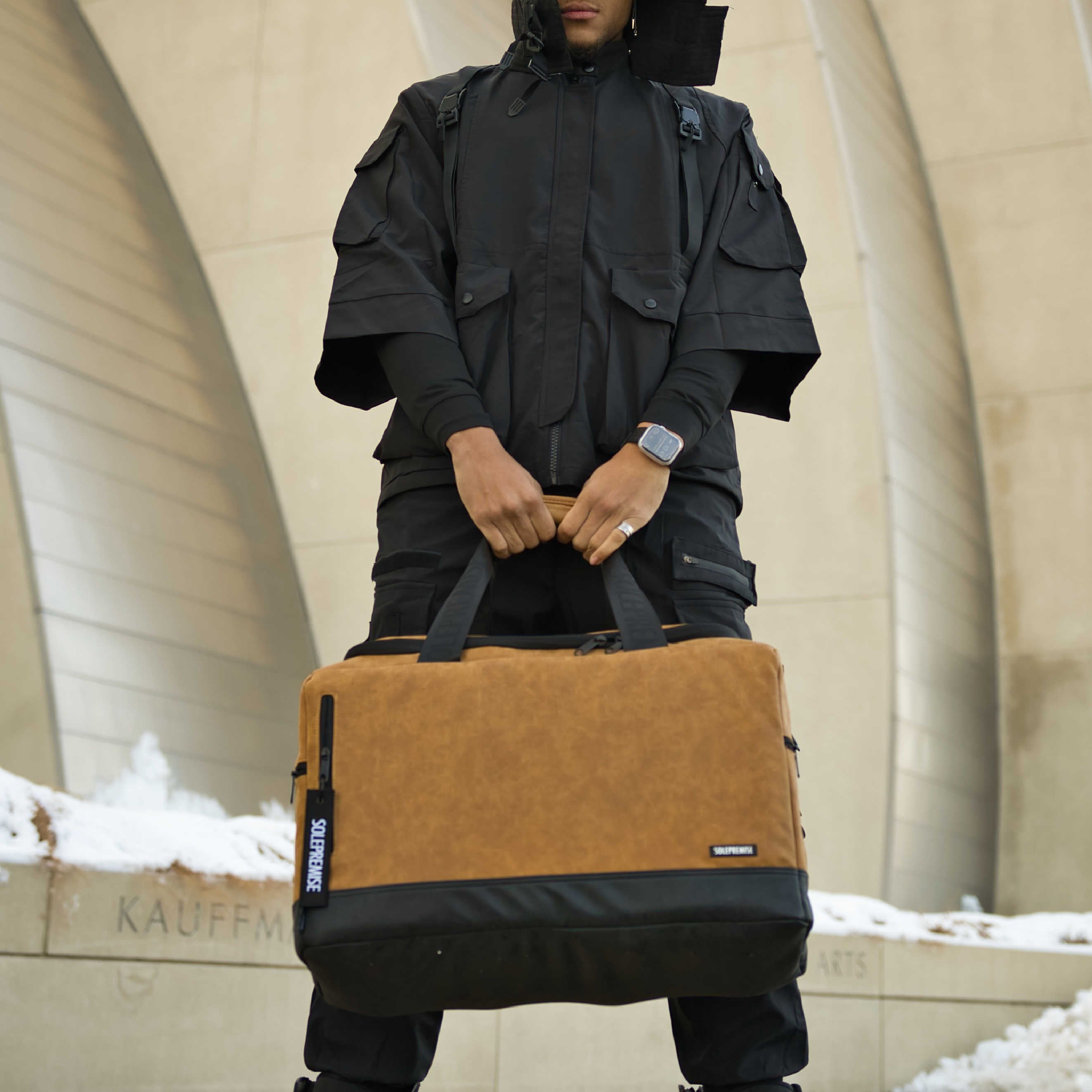 Person holding a brown and black bag in front of a building with snow on the ground