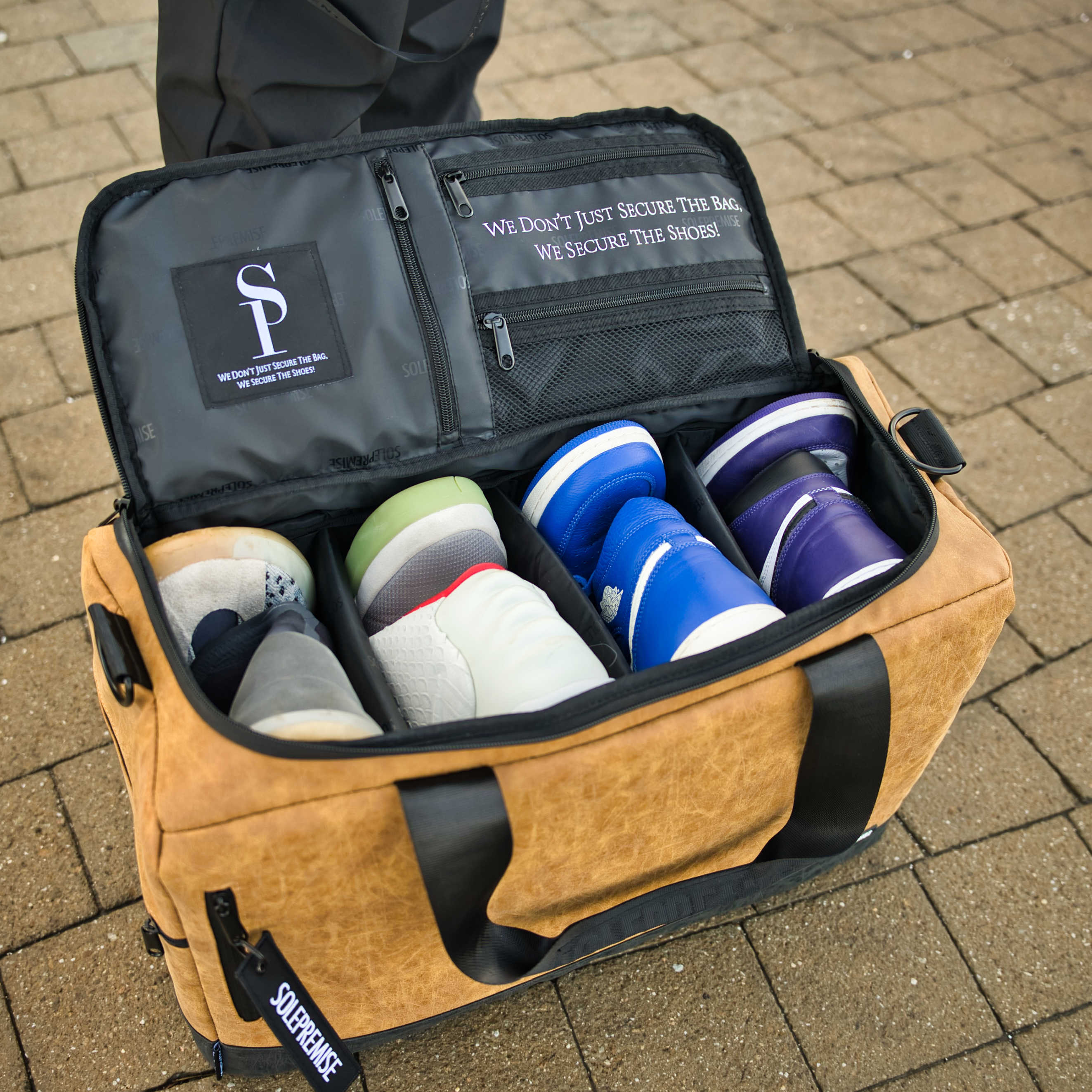 Brown shoe bag with multiple pairs of shoes on a brick surface