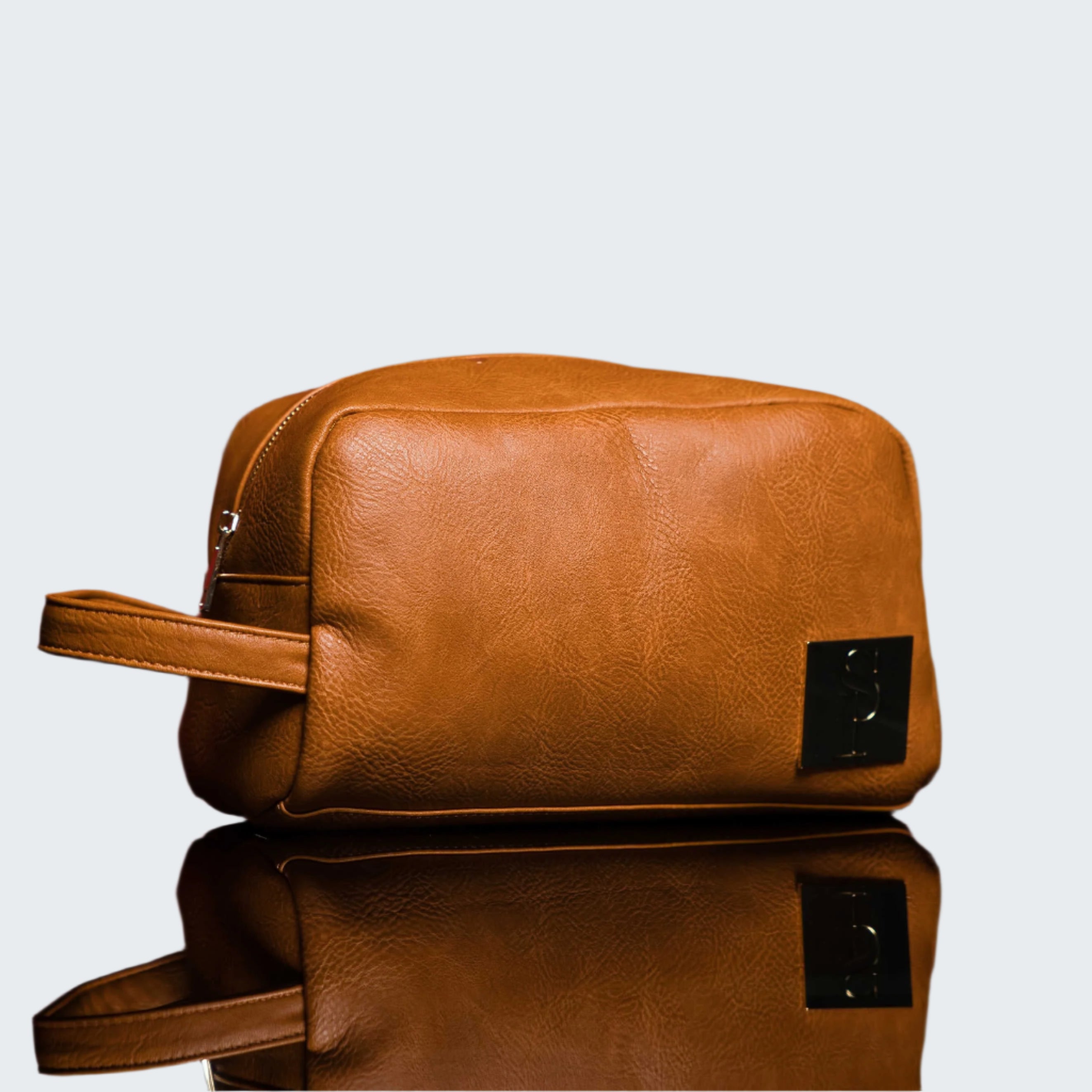Brown leather toiletry bag on a reflective surface with a red background