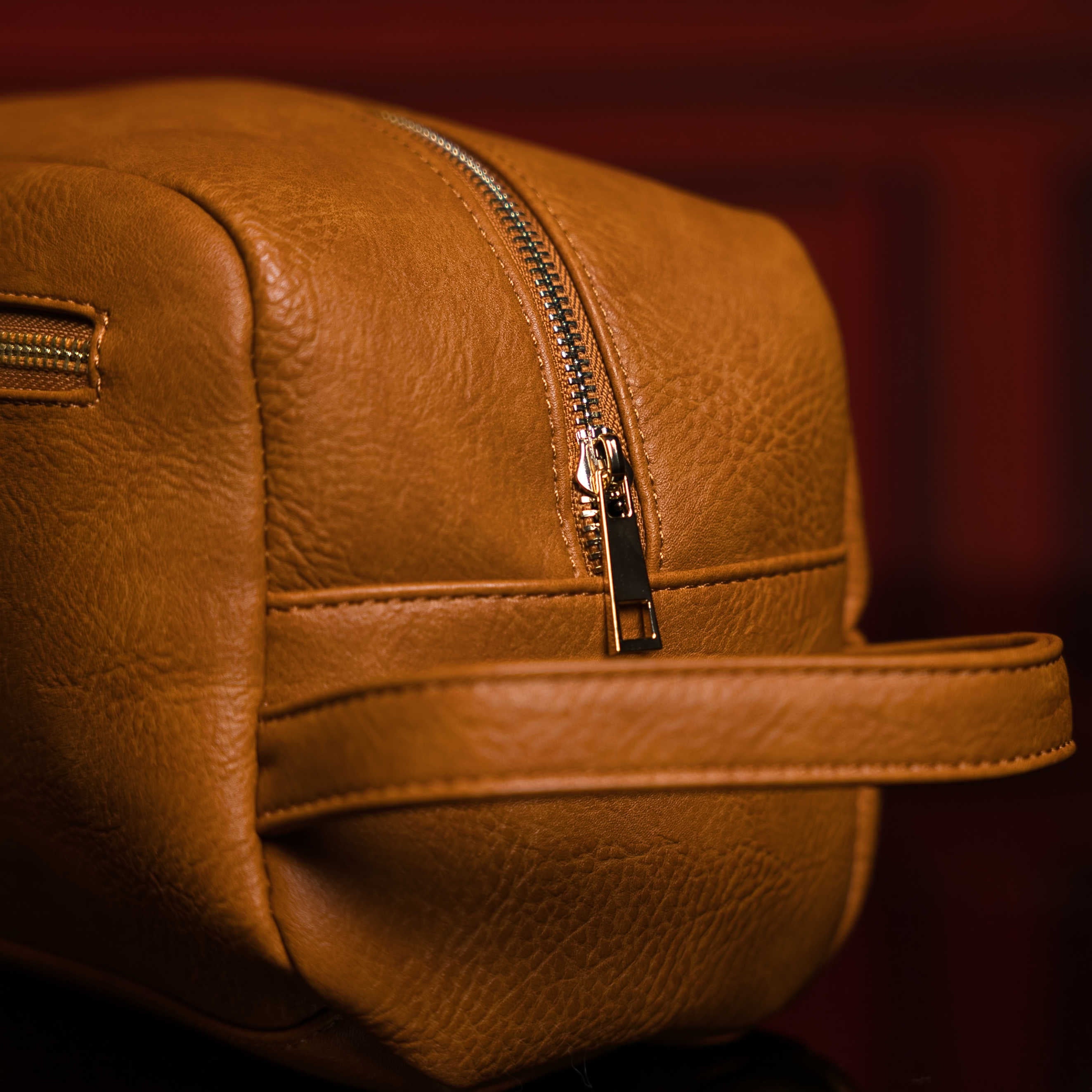 Close-up of a brown leather bag with a zipper on a dark background