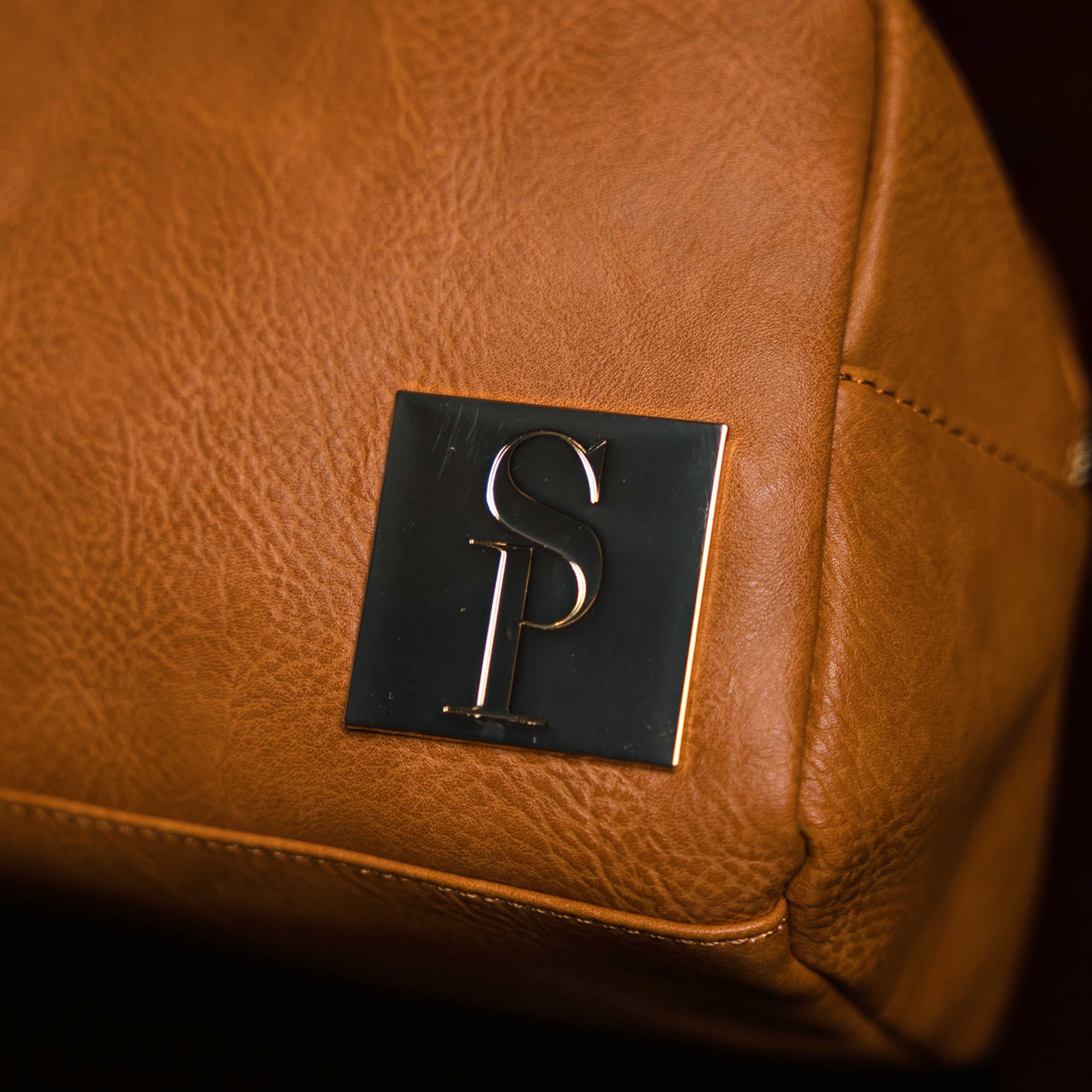 Close-up of a brown leather bag with a logo on a dark background
