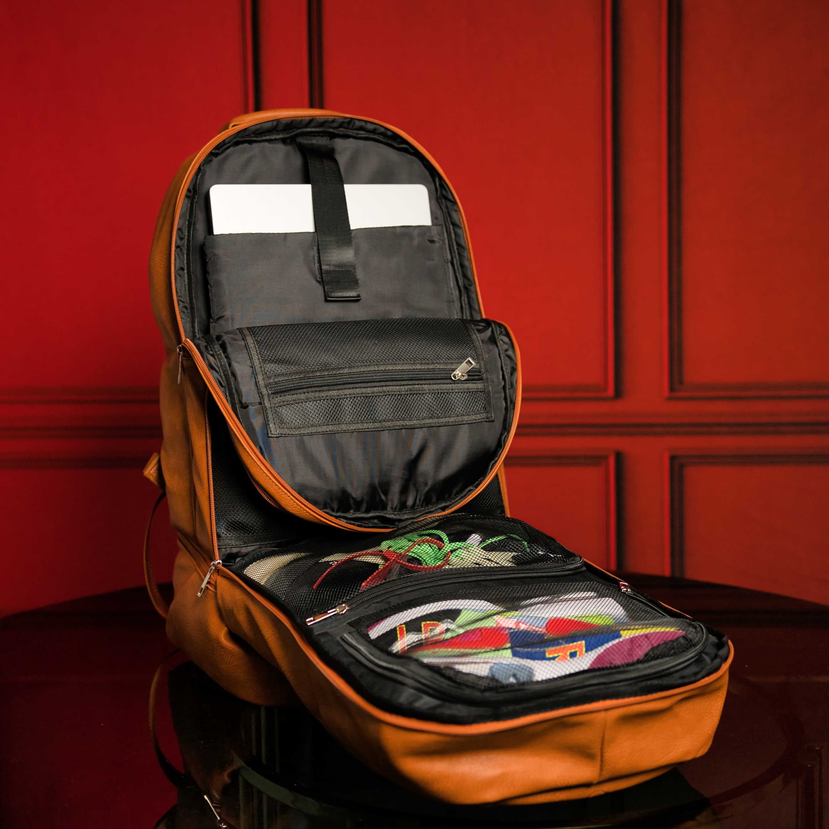 Open orange backpack with colorful items on a red background