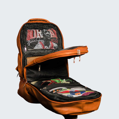 Open orange backpack with colorful contents against a red wall