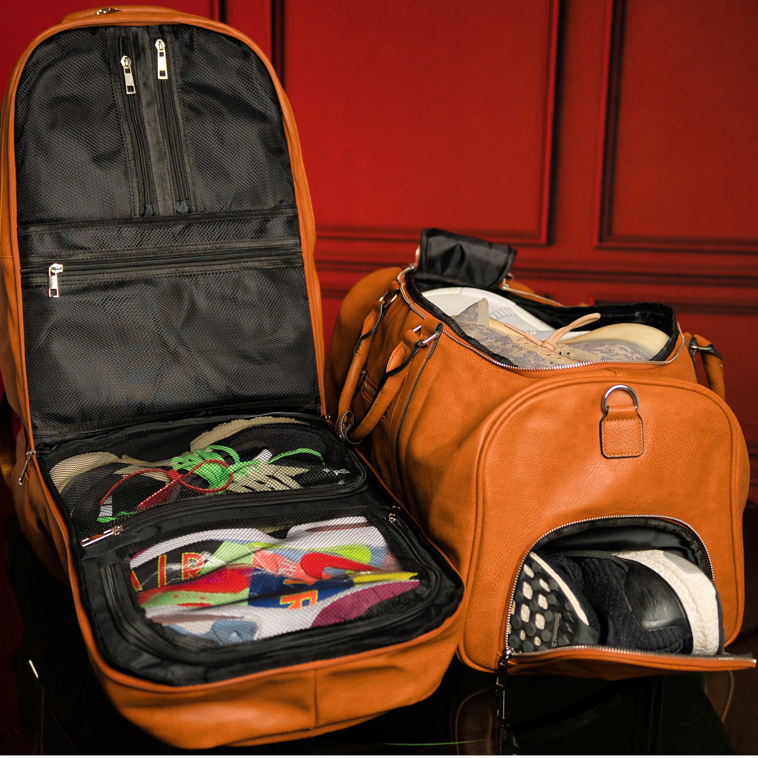Open orange travel duffel bag with clothes and shoes against a red background