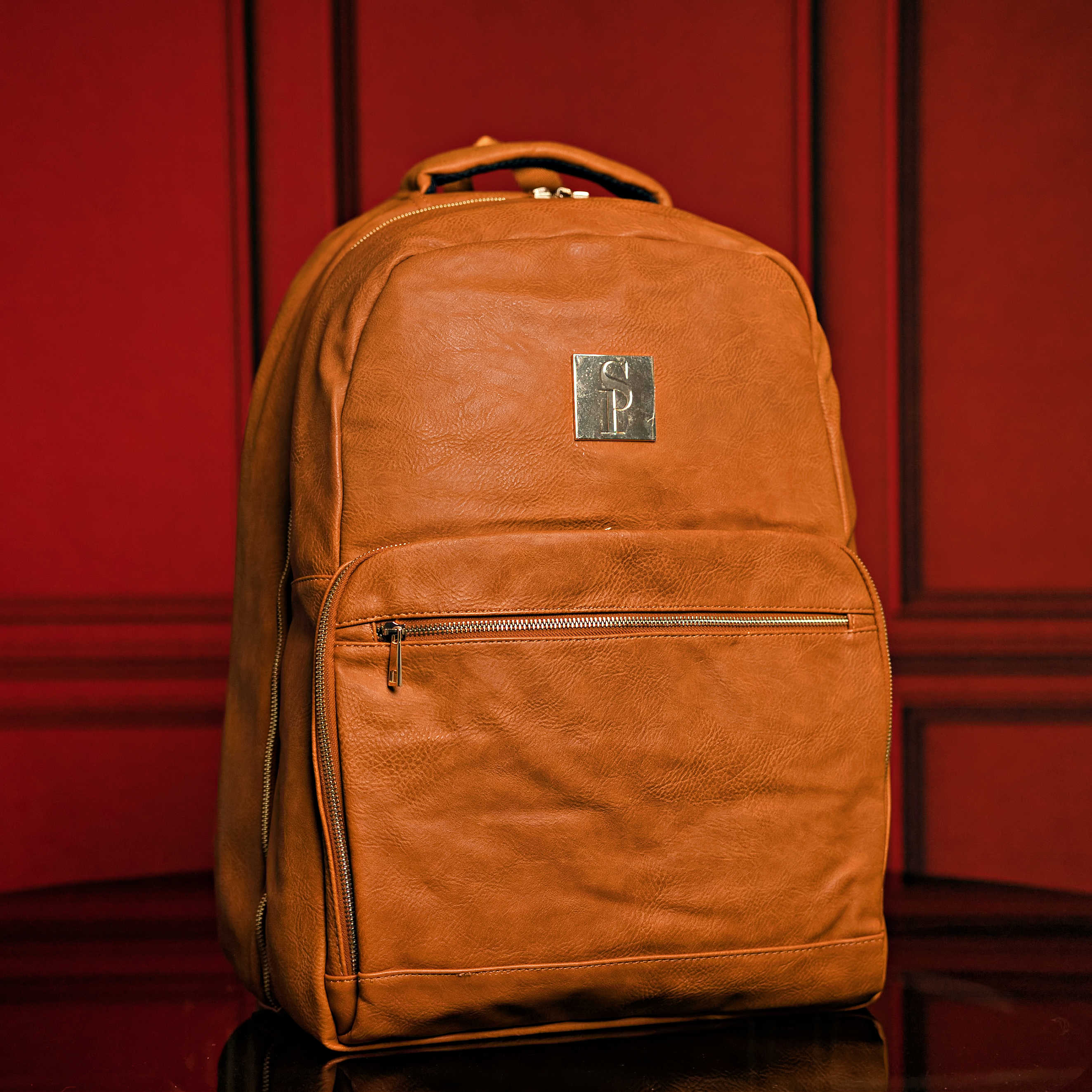Brown leather backpack with a brand logo on a red background