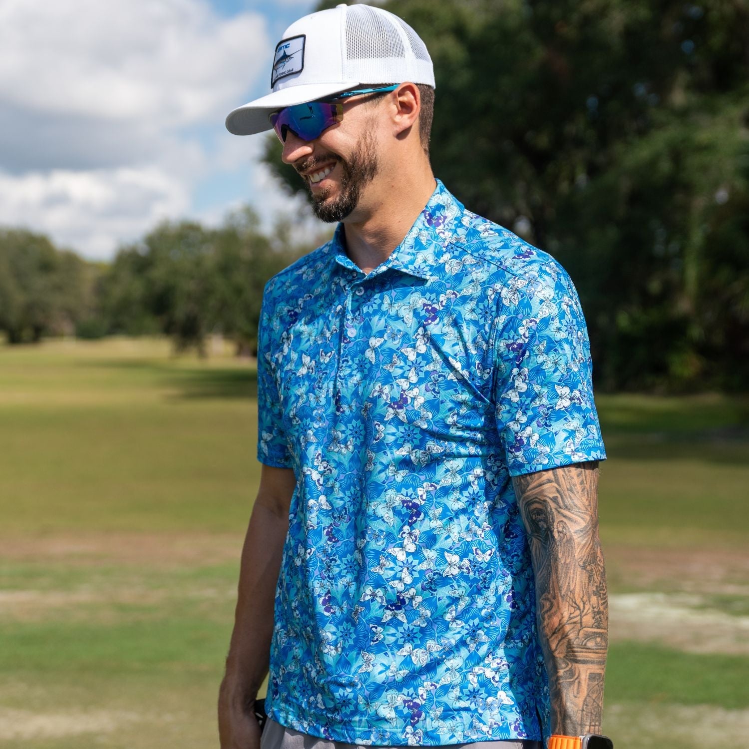 Man wearing a blue floral shirt and white cap on a golf course