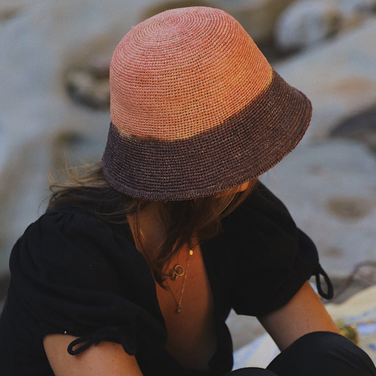 Person wearing a two-tone hat sitting on a sandy surface
