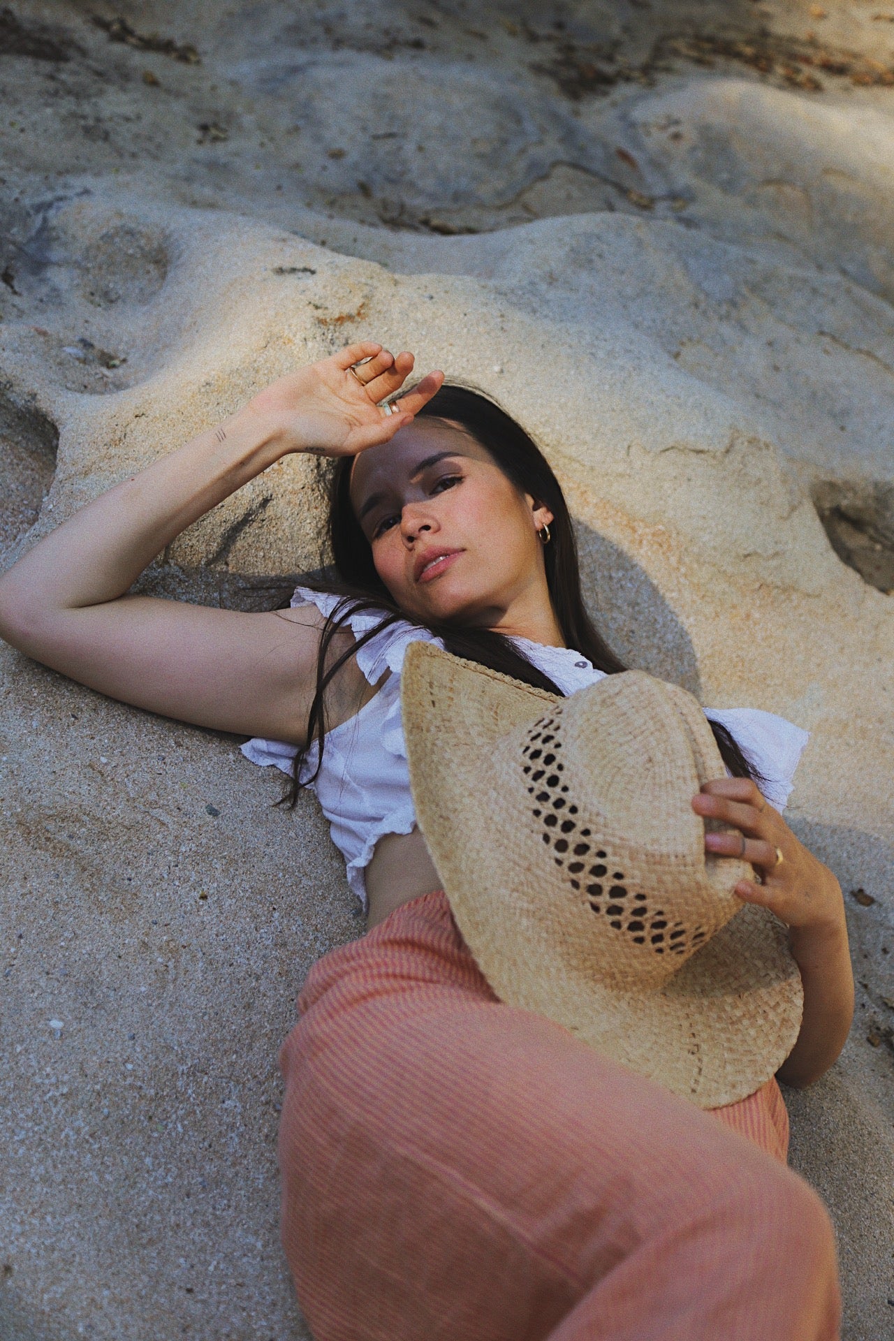Woman lying on sand holding a straw hat