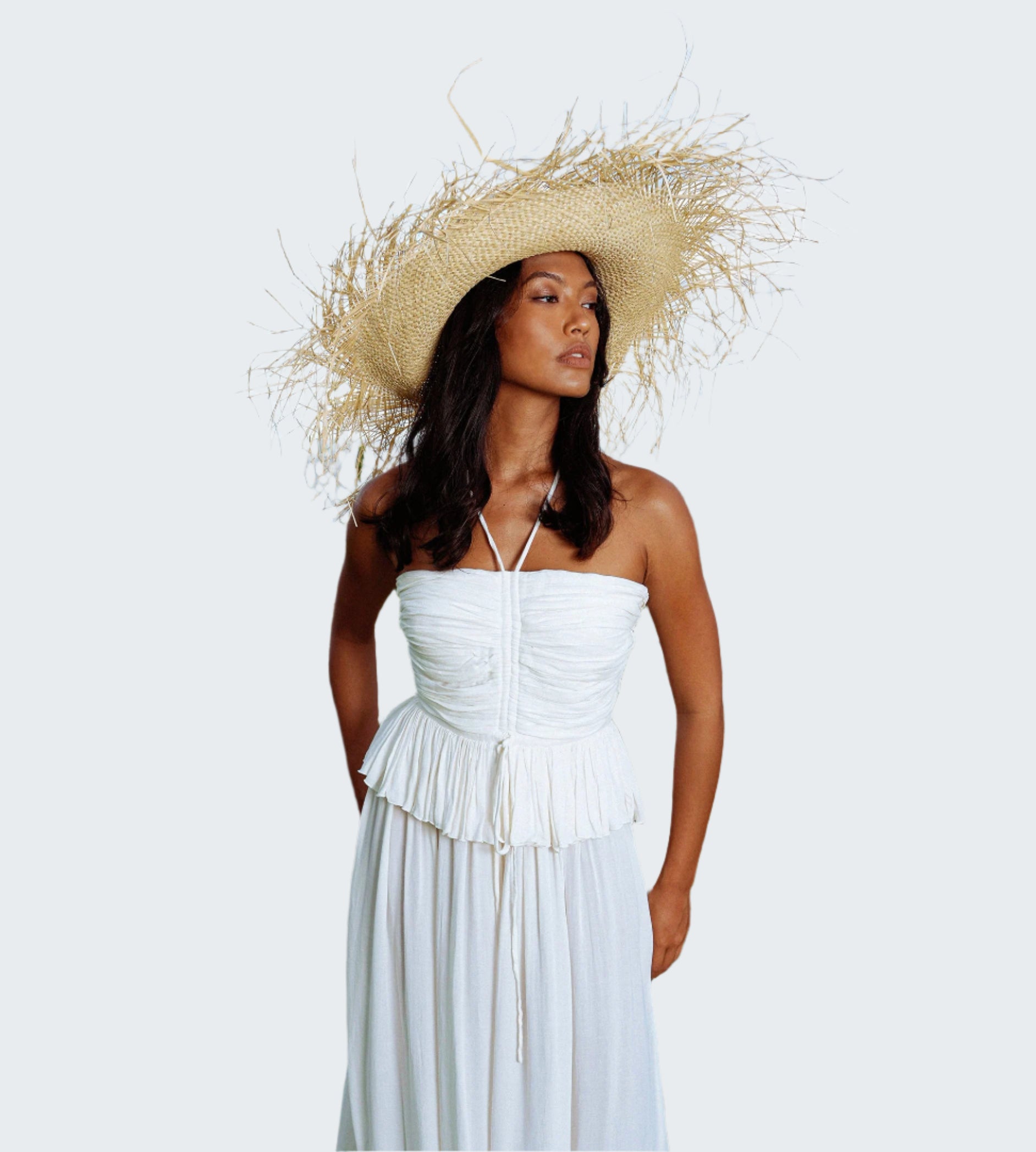 Woman in a white dress and straw hat standing outdoors with ocean in the background