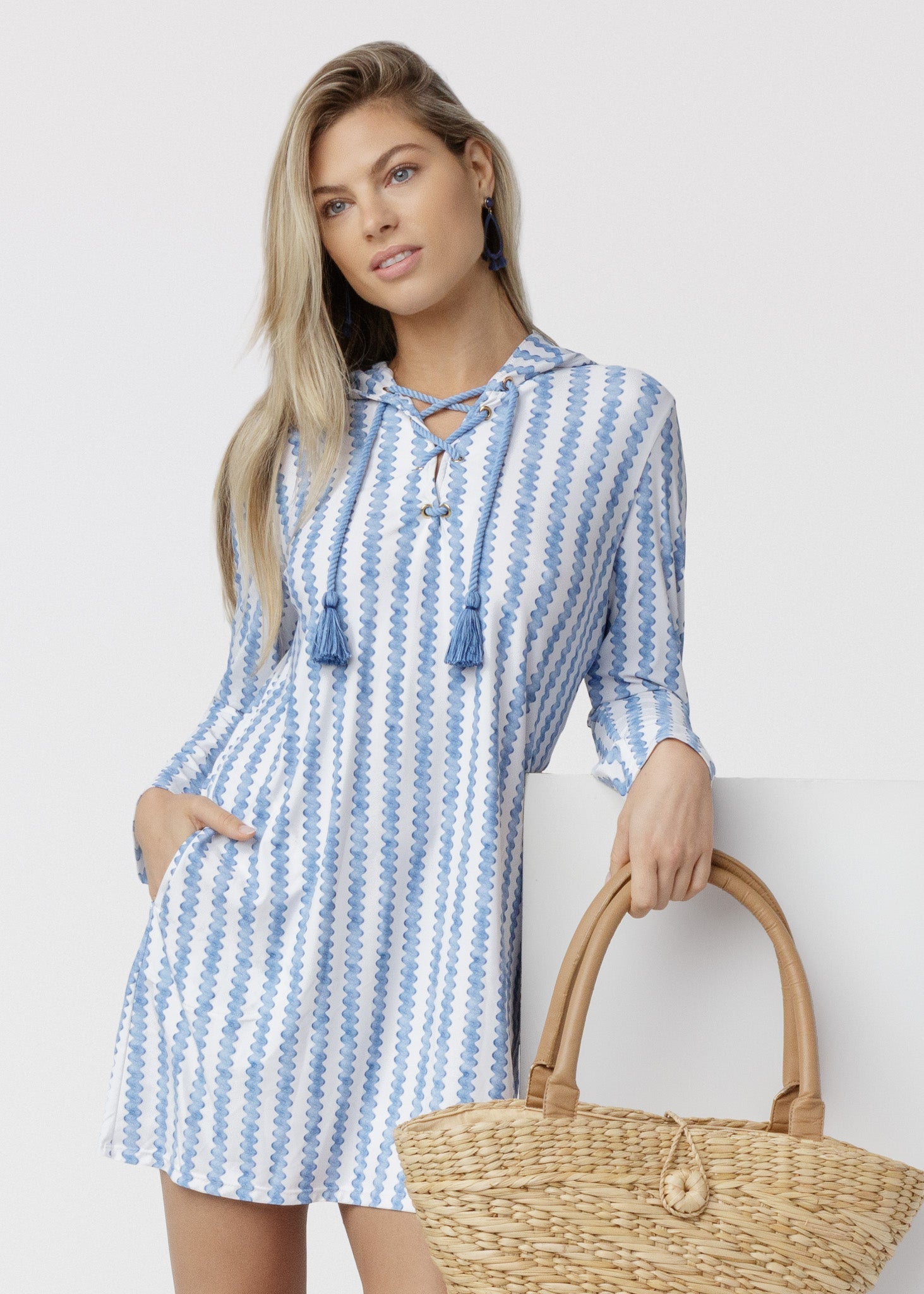 Woman wearing a blue and white striped dress holding a straw bag against a white background