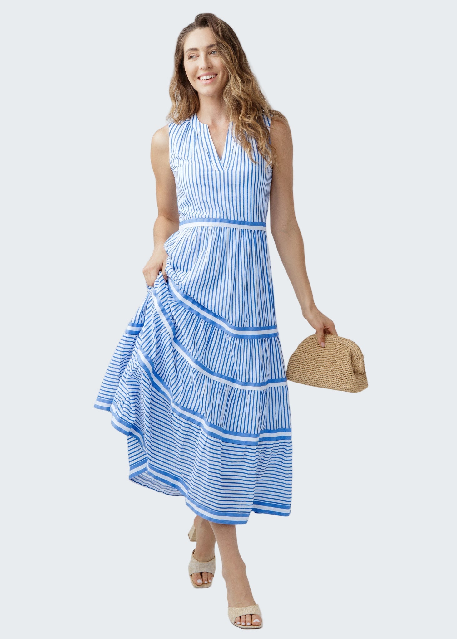 Woman wearing a blue and white striped dress holding a straw bag on a white background