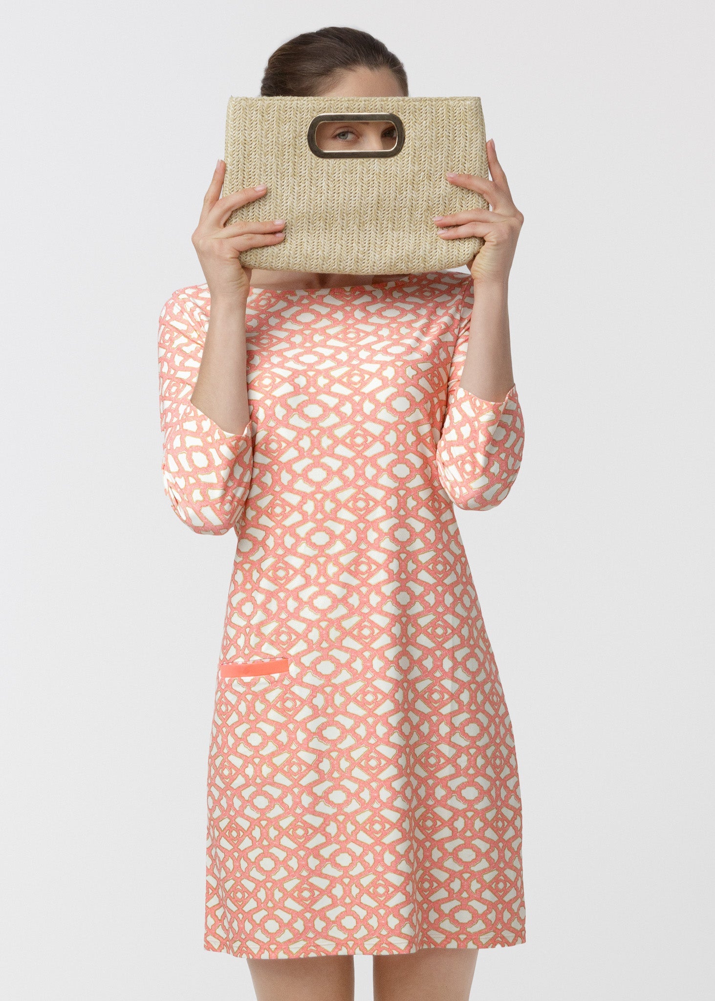 Woman wearing a patterned dress holding a woven bag against a white background
