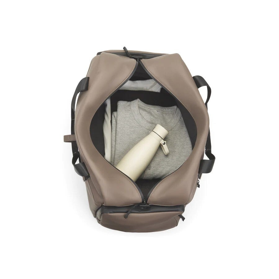 Brown duffel bag with clothes and a bottle on a white background