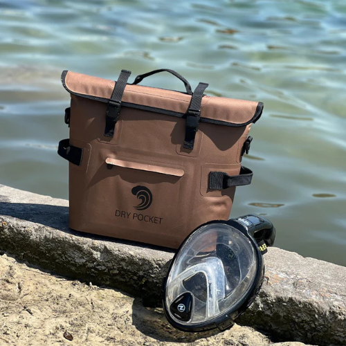 Brown waterproof bag with 'Dry Pocket' logo and a black flashlight on a rock by water.