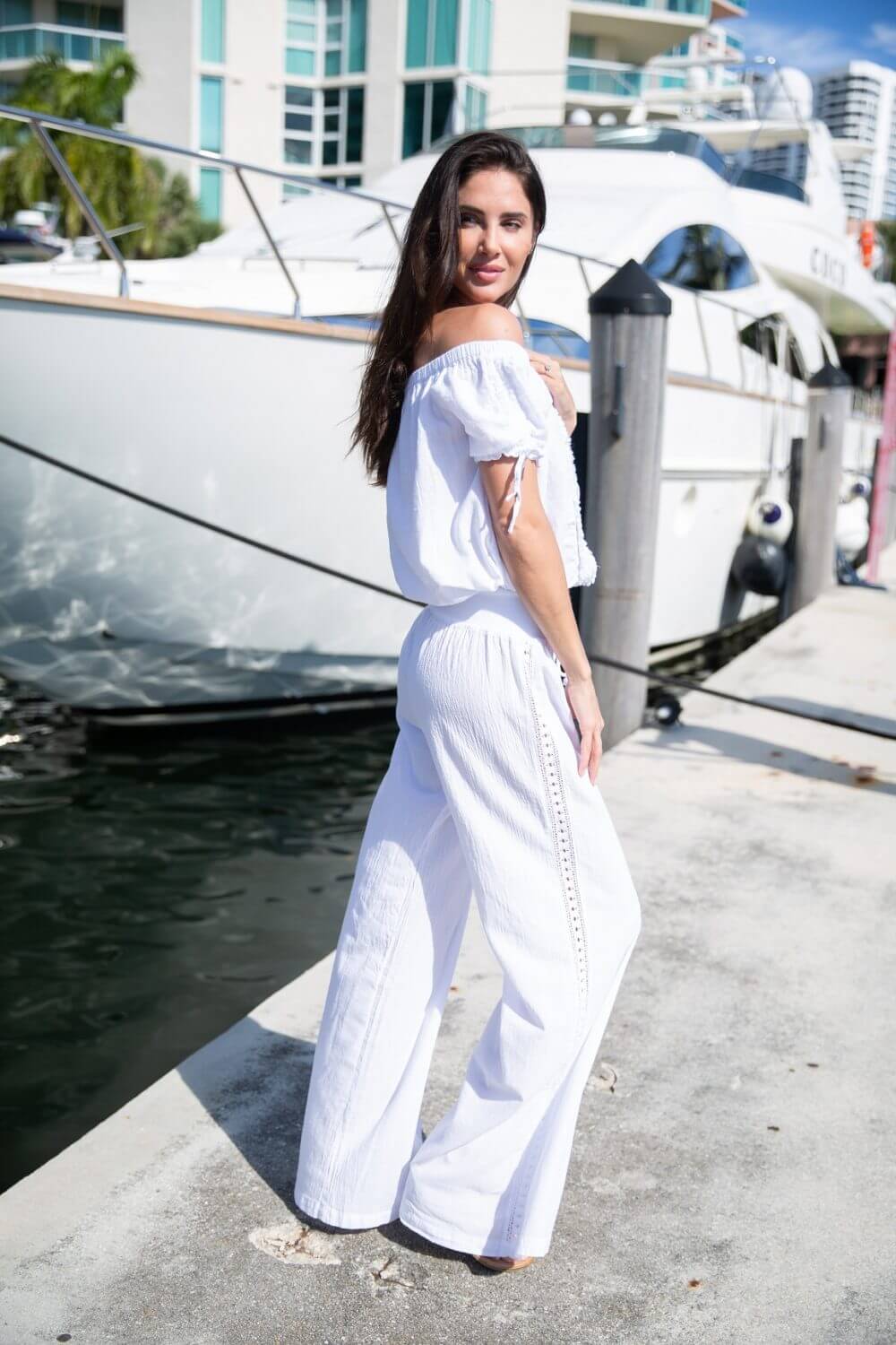Woman in a white outfit standing by a dock with yachts in the background