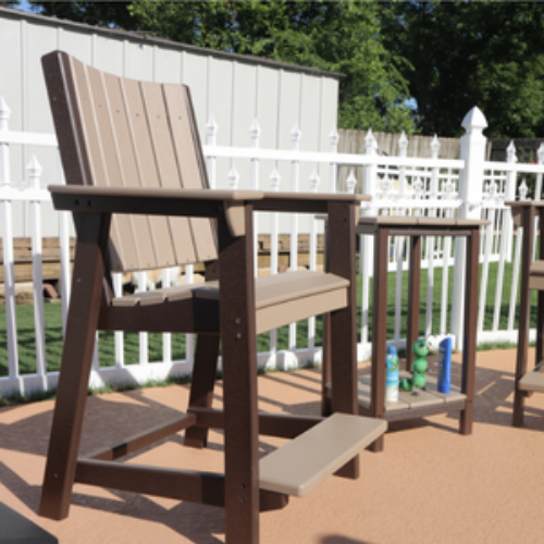 Wooden chair with a step on a deck with a white fence and greenery in the background