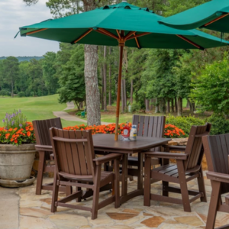 Outdoor dining set with wooden chairs and table under a green umbrella in a garden setting.