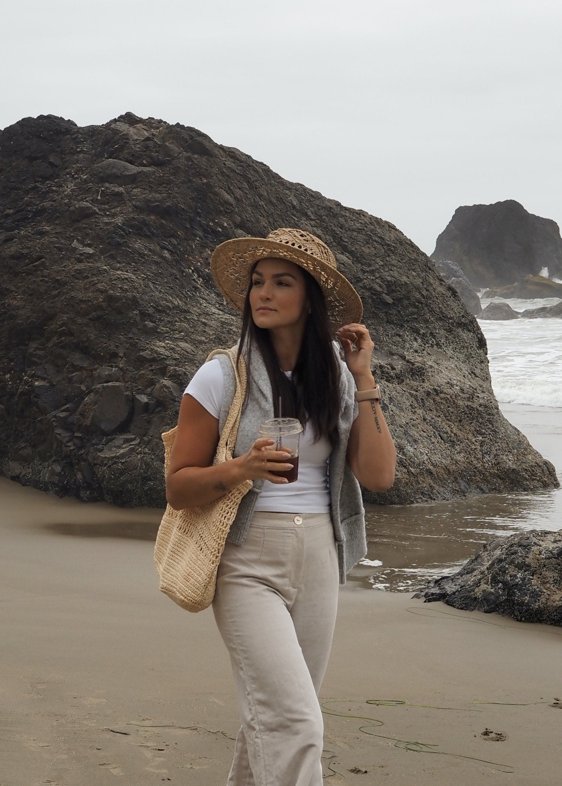 Woman standing on a beach with large rocks and ocean in the background