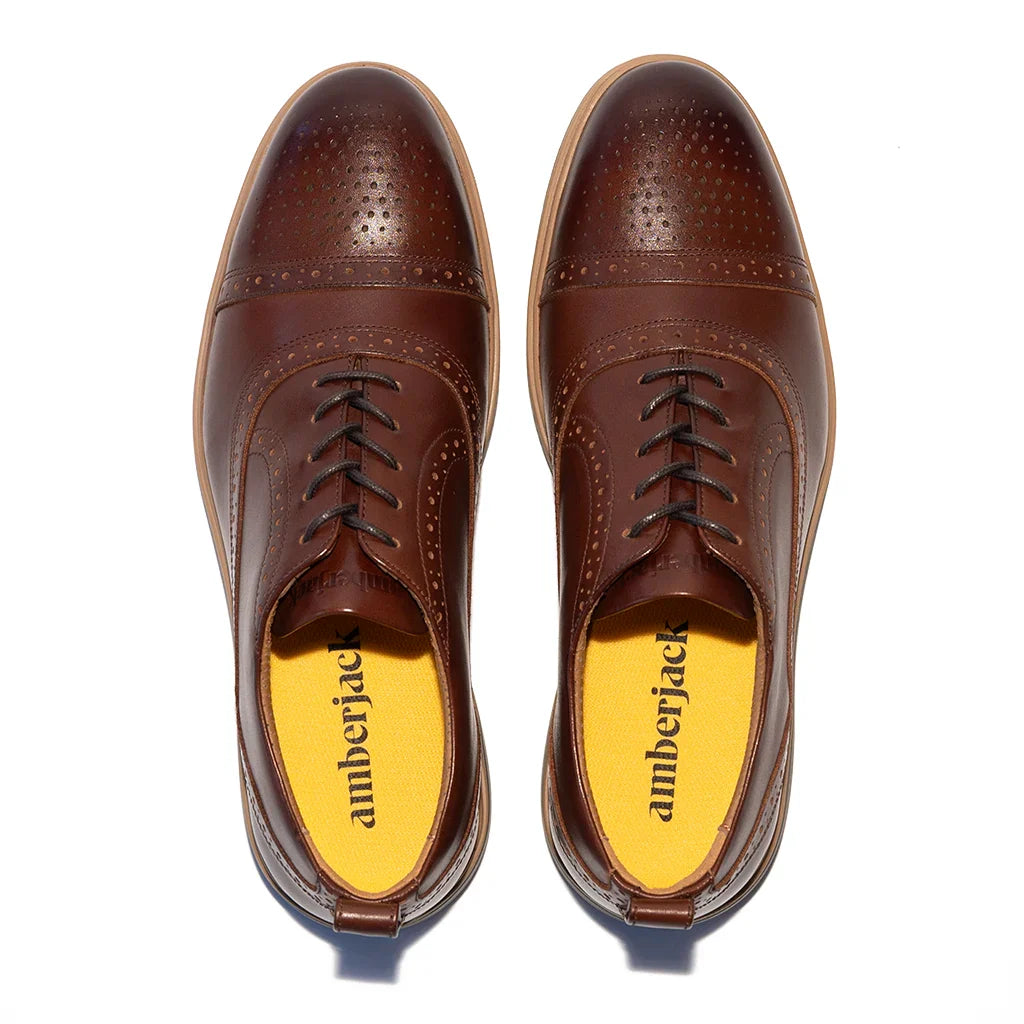 Pair of brown leather shoes with yellow soles on a white background