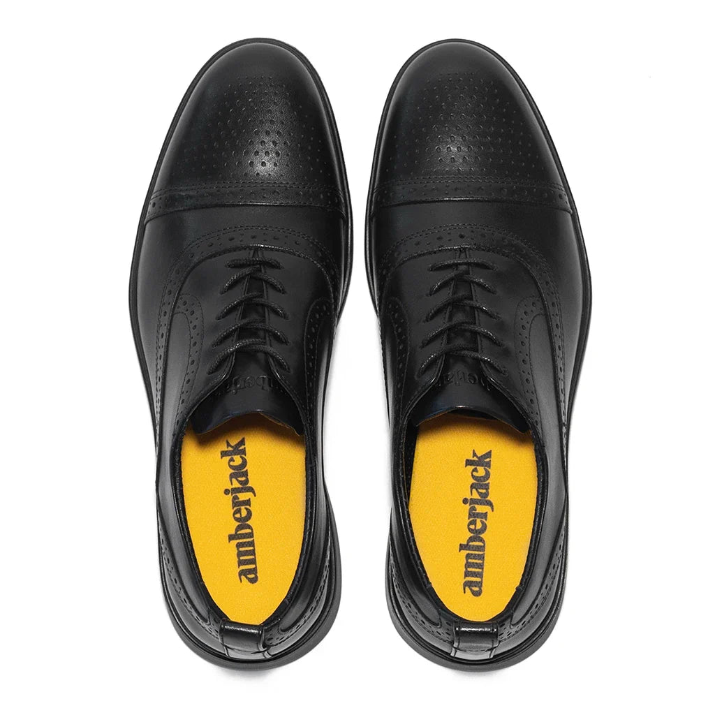Black dress shoes with yellow soles on a white background