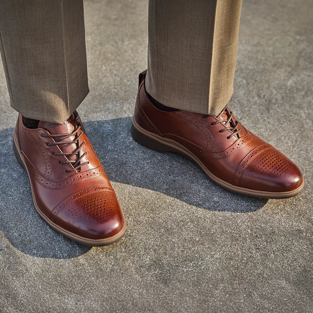 Brown leather dress shoes worn with beige pants on a concrete surface