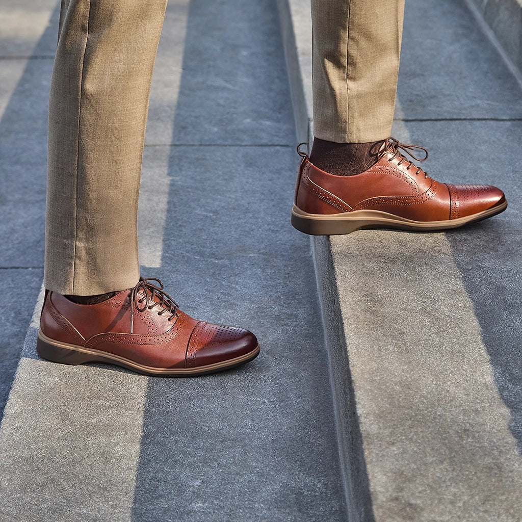 Brown leather shoes worn with beige pants on a concrete surface