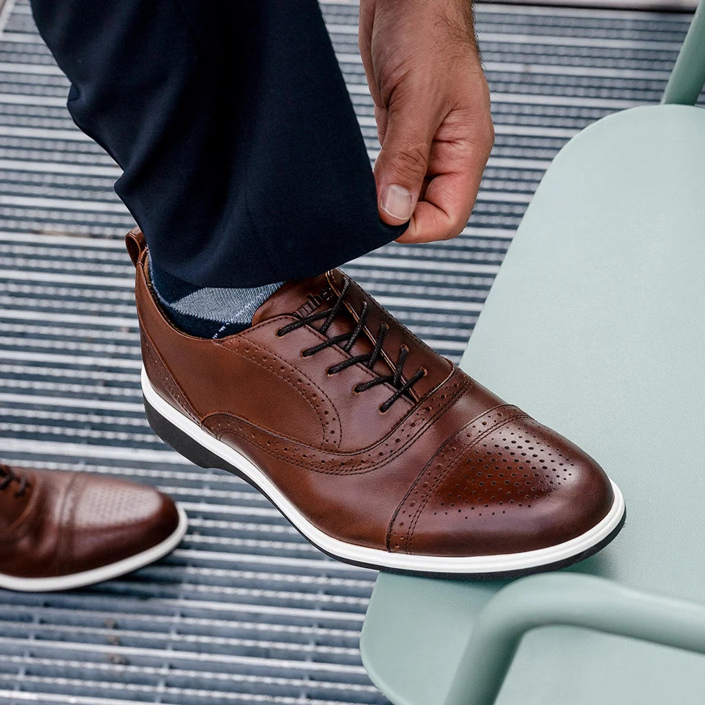 Brown leather shoes with white soles worn by a person sitting on a light blue chair.