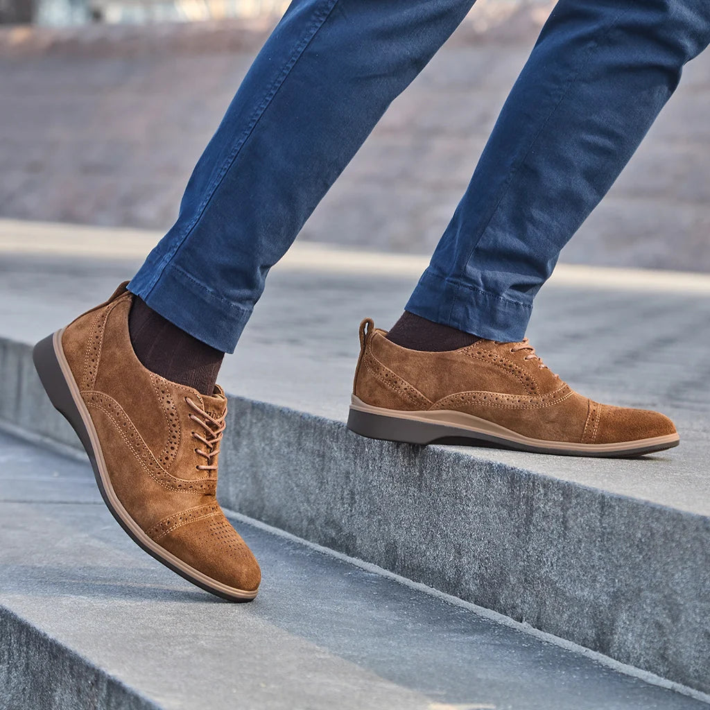 Brown suede shoes worn with blue jeans on a concrete staircase.