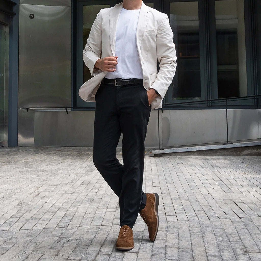 Person wearing a white blazer, black pants, and brown shoes standing on a paved area.