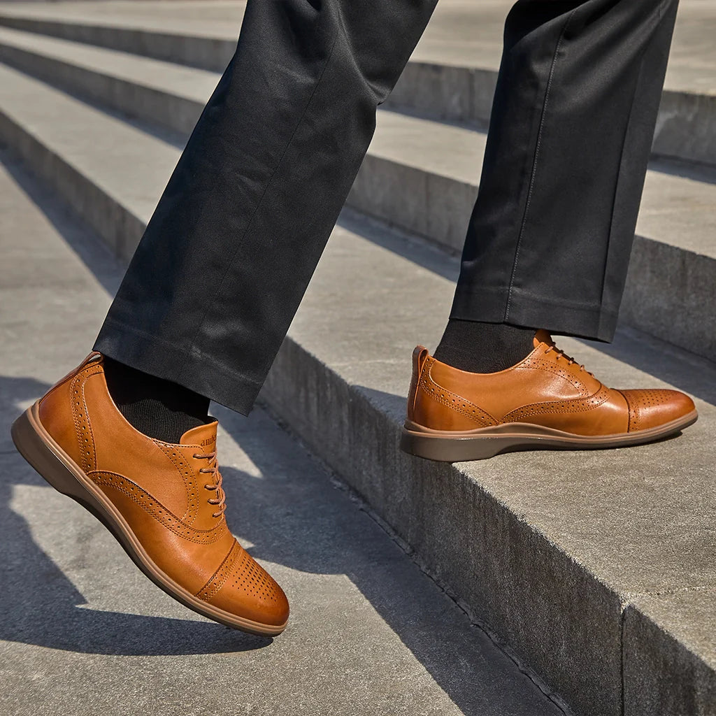 Brown leather shoes worn with dark pants on a concrete surface