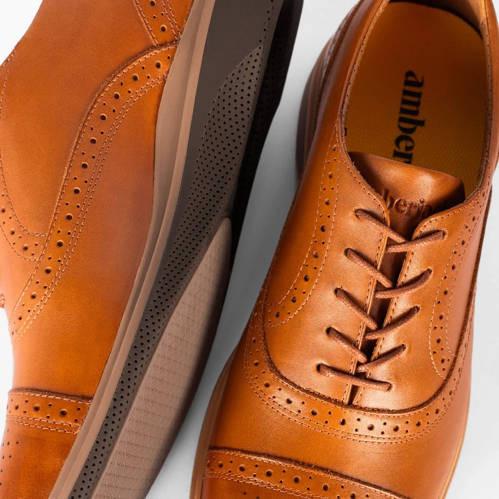 Brown leather dress shoes with detailed sole on a light gray background