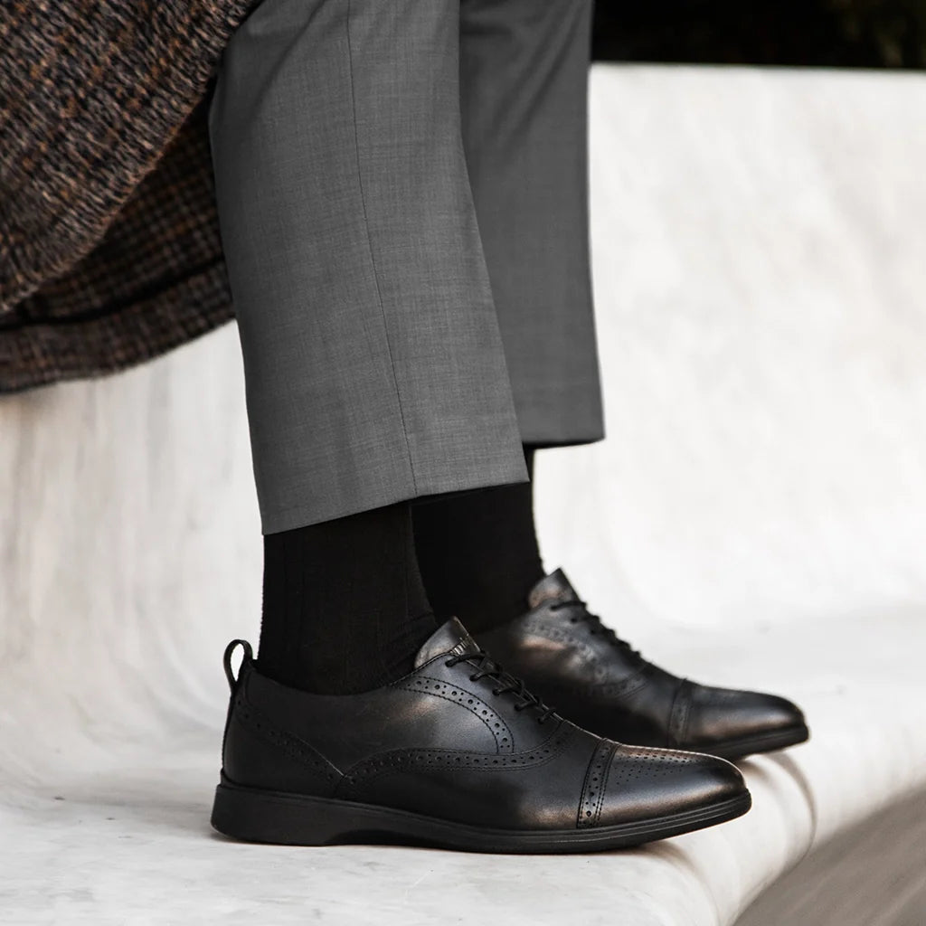 Person wearing black dress shoes and gray pants on a light background