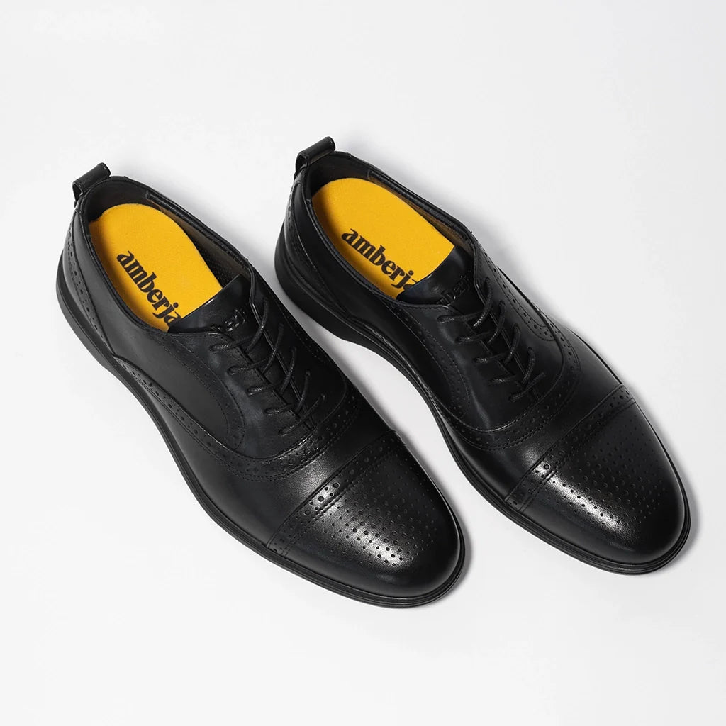 Black dress shoes with yellow soles on a white background