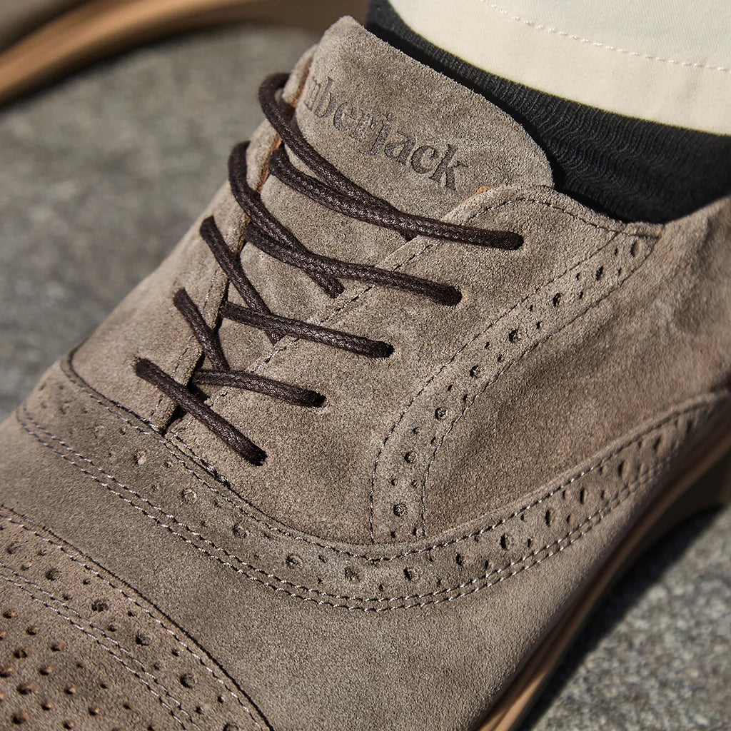 Close-up of a gray suede shoe with brown laces on a concrete surface