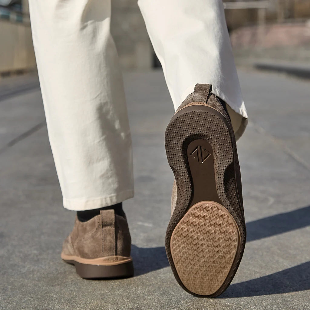 Brown sandals worn with white pants on a concrete surface