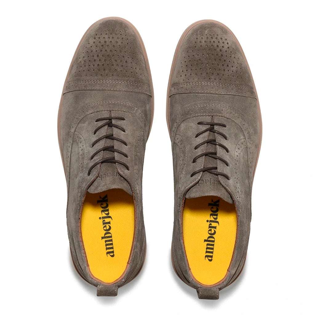 Pair of gray suede shoes with yellow lining on a white background