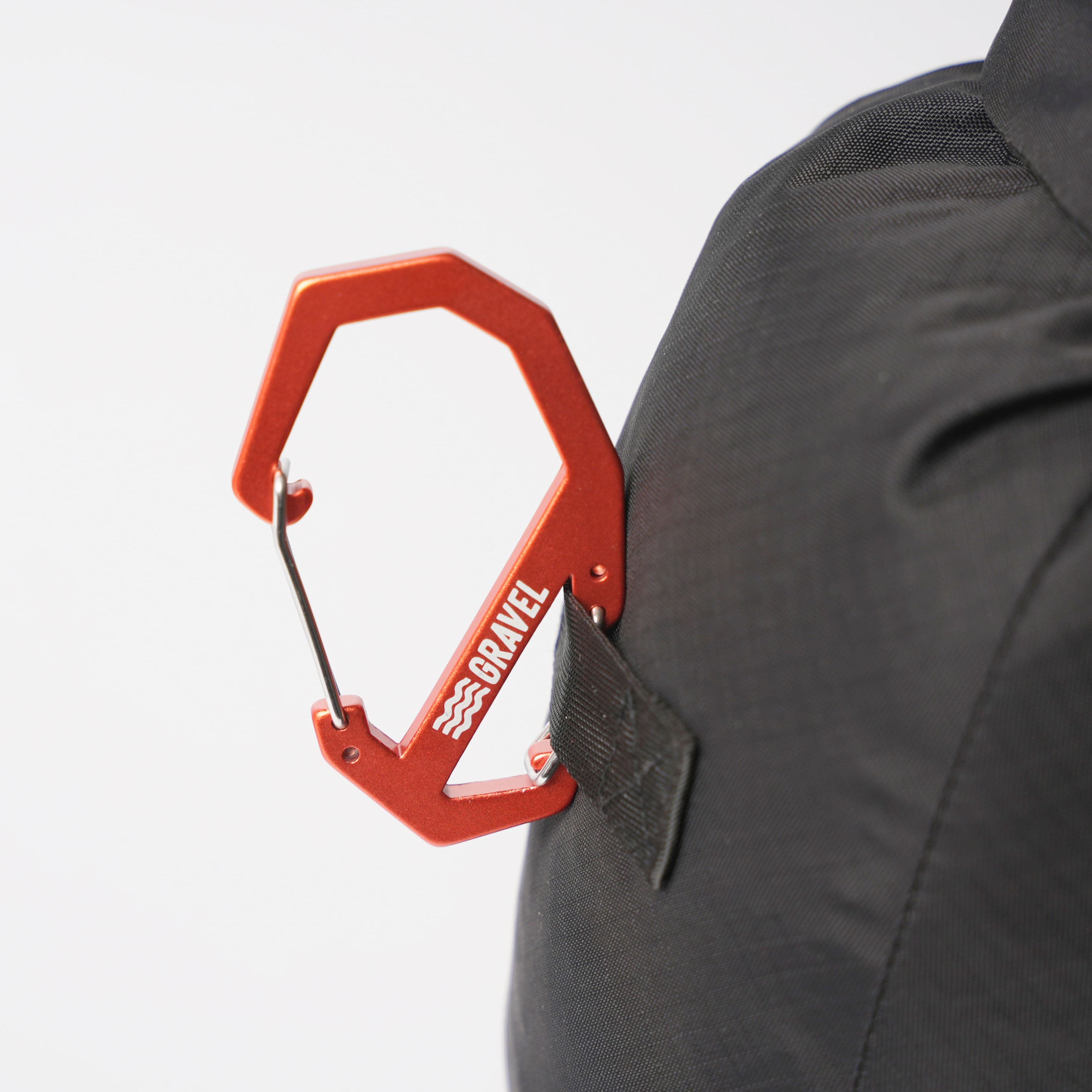 Orange carabiner attached to a black backpack on a white background